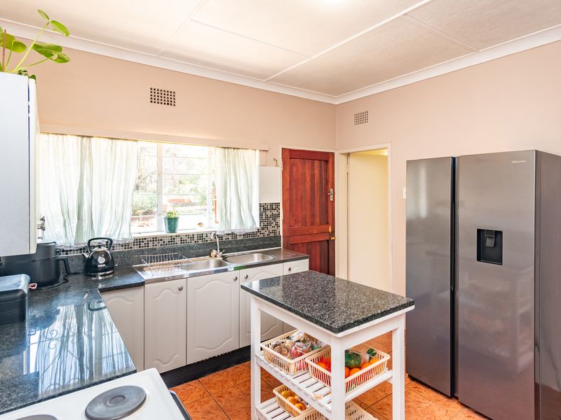 Functional kitchen featuring granite countertops, mosaic tile backsplash, double sink, and tiled flooring, offering a practical layout for daily meal preparation.