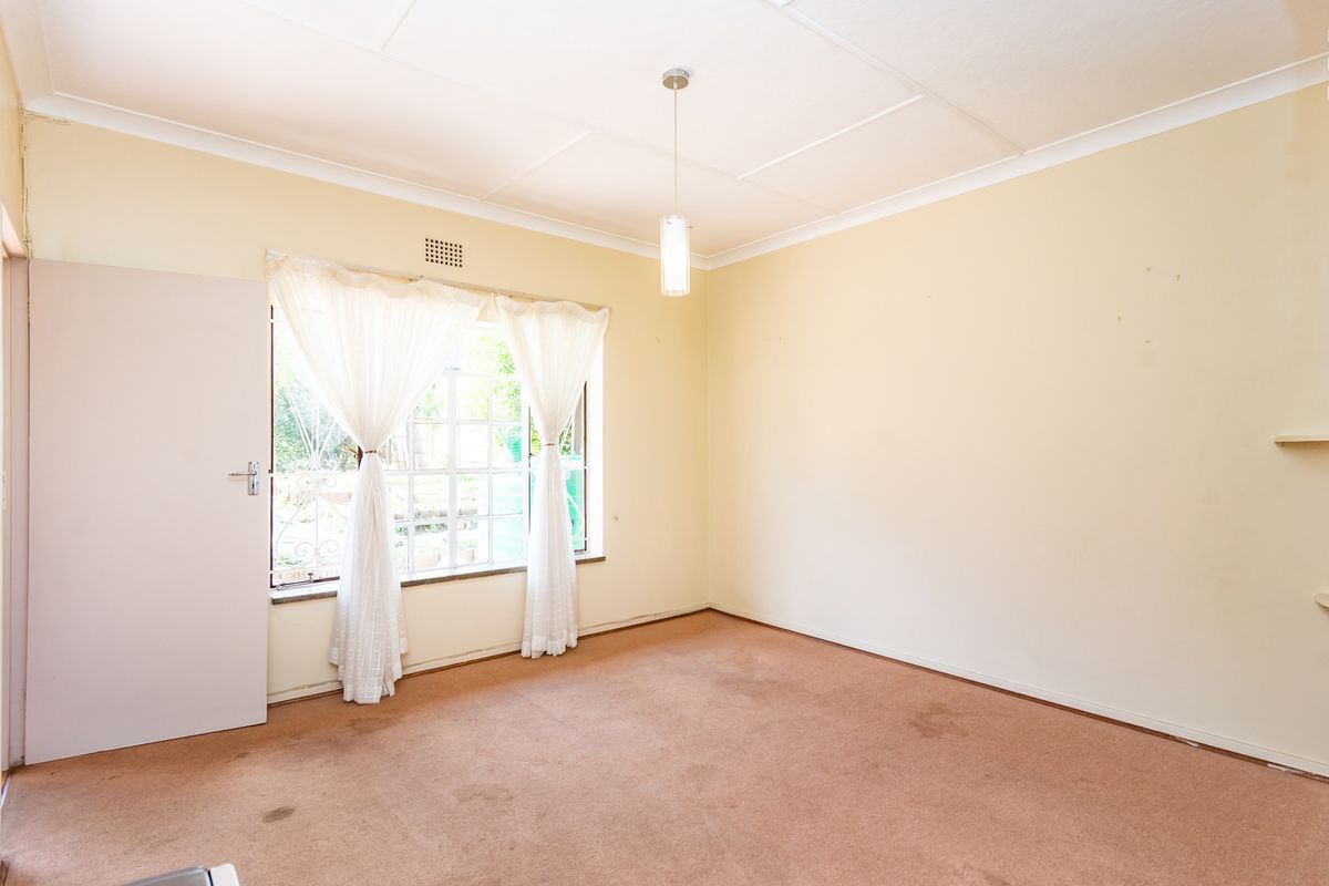 An empty bedroom featuring carpeted flooring, a pendant light fixture, and a window with natural light.