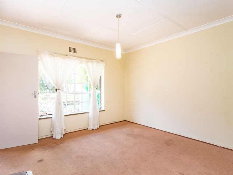 An empty bedroom featuring carpeted flooring, a pendant light fixture, and a window with natural light.