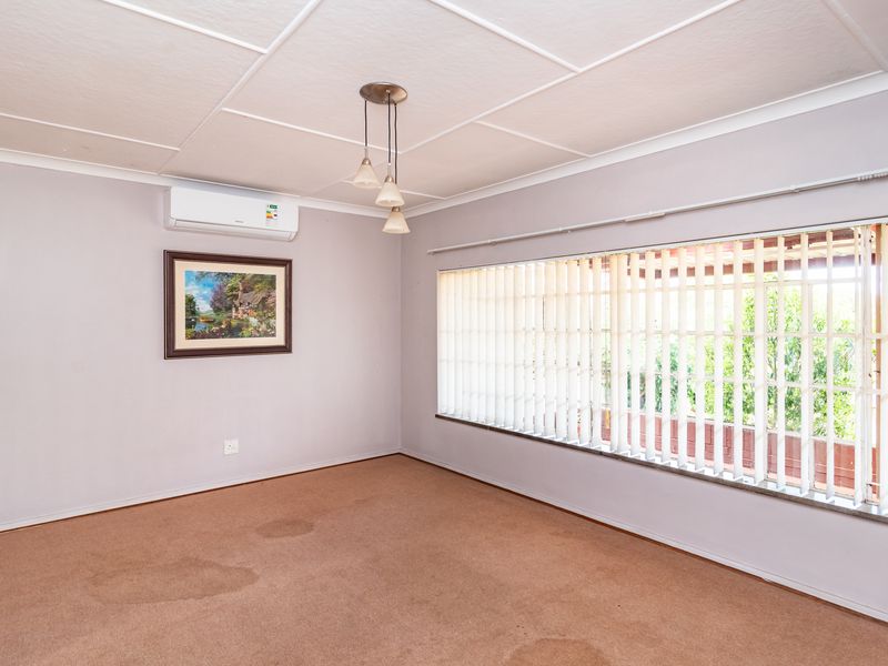A spacious, empty living room featuring carpeted flooring, a split-system air conditioner, and large windows with vertical blinds.