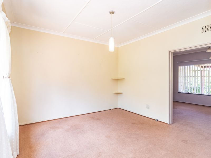 An empty living room featuring neutral walls, carpet flooring, and built-in corner shelving, with an open doorway leading to an adjacent room.