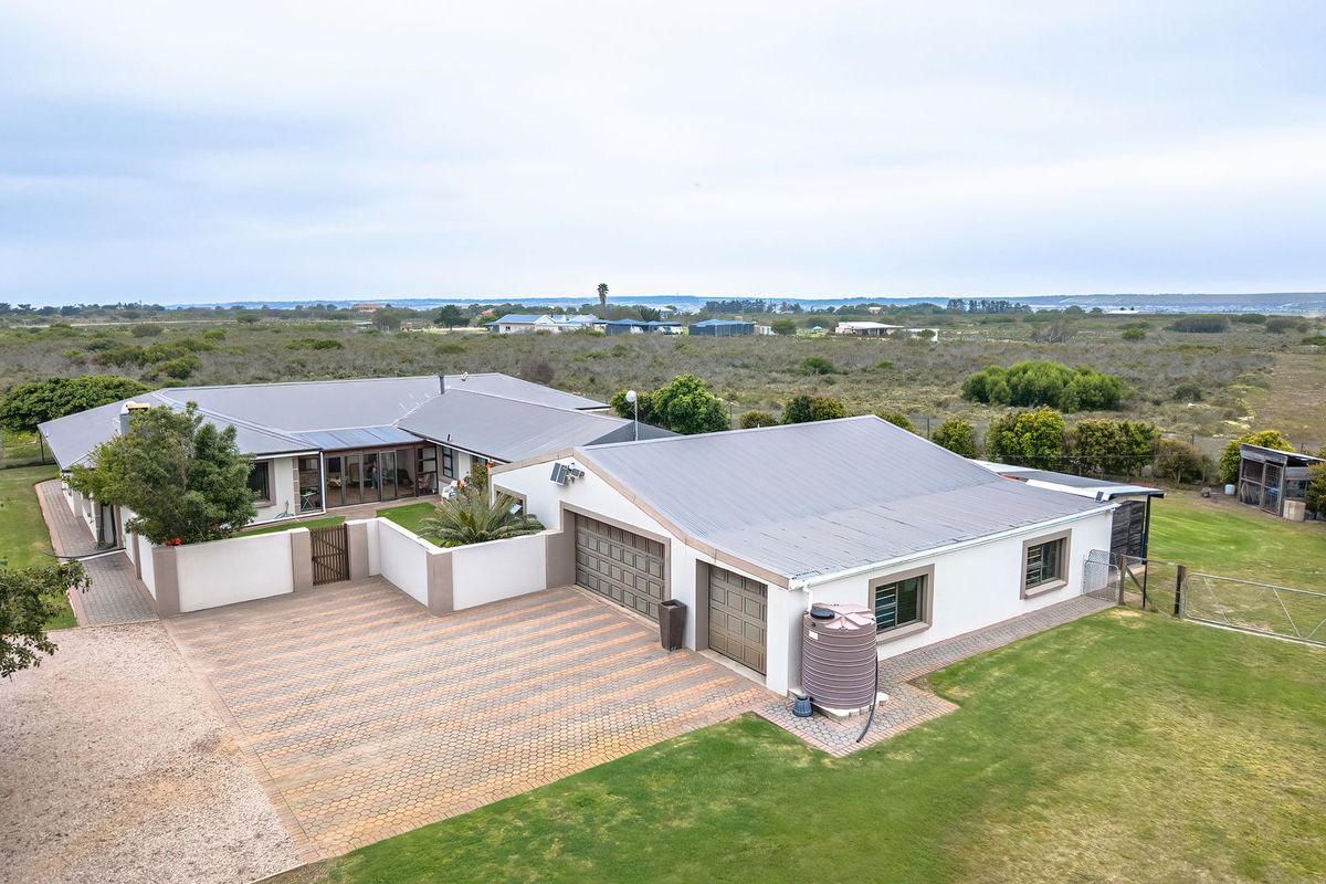 Aerial view of a well-maintained small holding featuring a spacious residence with a double garage, paved driveway, and expansive surrounding garden grounds.