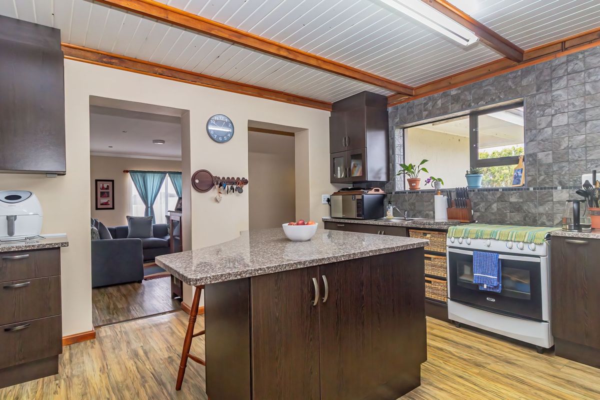 A well-maintained kitchen featuring dark wood cabinetry, granite countertops, a central island, and a tiled backsplash, with an open flow to the living area.