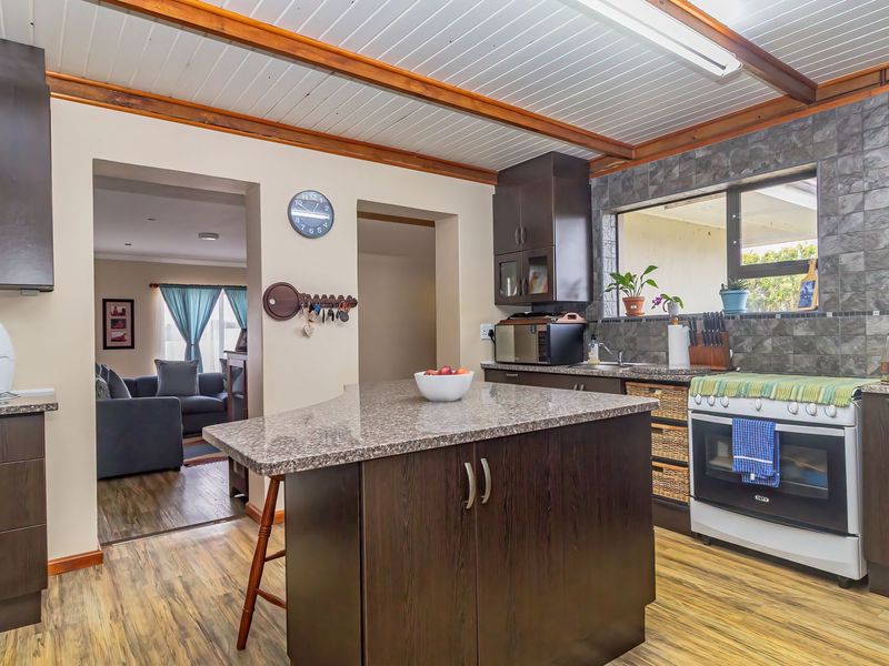 A well-maintained kitchen featuring dark wood cabinetry, granite countertops, a central island, and a tiled backsplash, with an open flow to the living area.