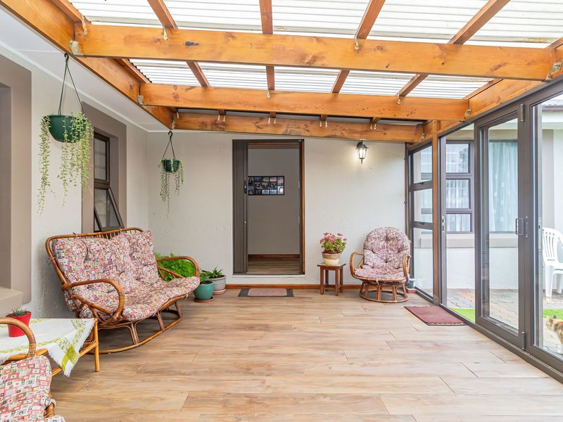 A covered patio area featuring a timber pergola with translucent roofing, tiled floors, and large aluminium sliding doors providing access to the garden.