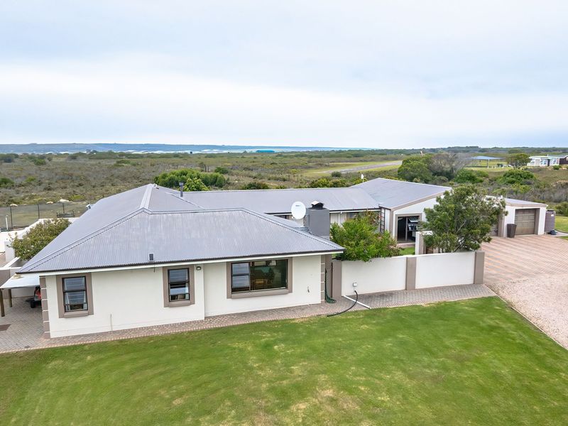 Aerial view of a well-maintained small holding property featuring a main residence with a metal roof, paved driveway, garage, and expansive surrounding grounds.
