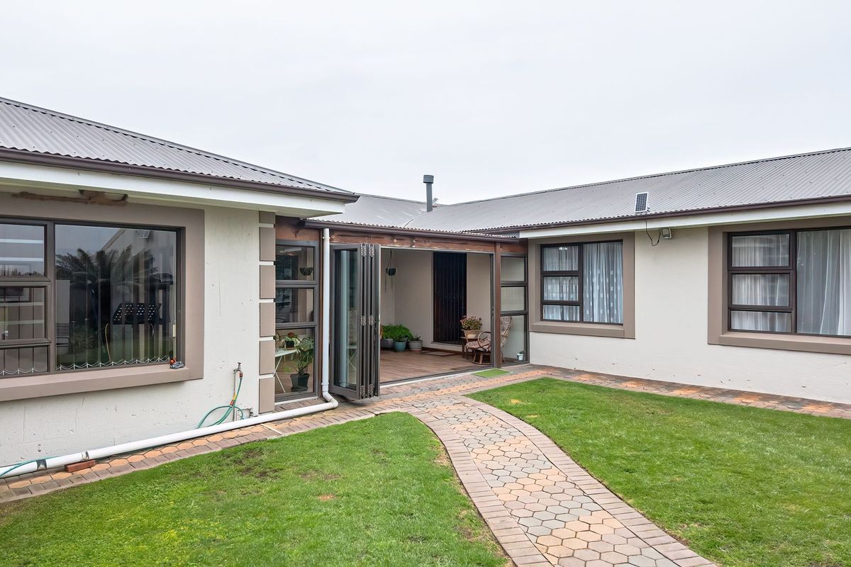 Rear view of the property featuring a paved walkway, well-maintained lawn, and a covered patio area with folding glass doors.
