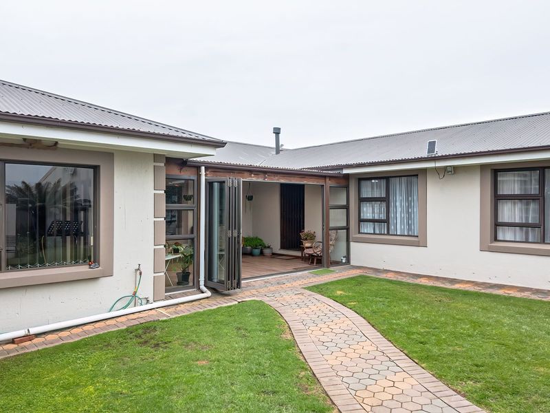 Rear view of the property featuring a paved walkway, well-maintained lawn, and a covered patio area with folding glass doors.