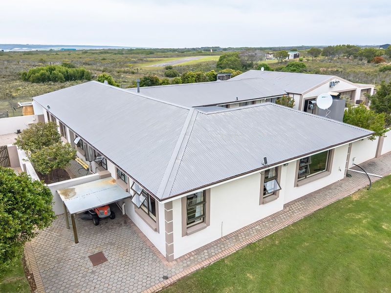 Aerial view of a single-story small holding property featuring a corrugated metal roof, paved outdoor areas, and surrounding landscaped grounds.