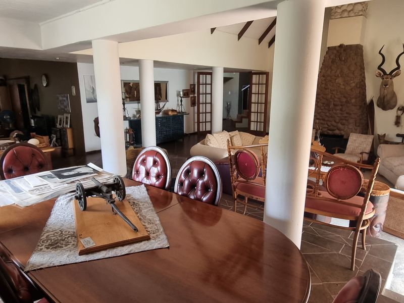Spacious open-plan living and dining area featuring a prominent stone fireplace, exposed timber ceiling beams, and tiled flooring throughout.
