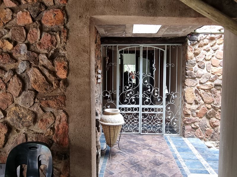 A rustic entrance area featuring natural stone walls, a decorative wrought iron security gate, and a covered patio space with tiled flooring.