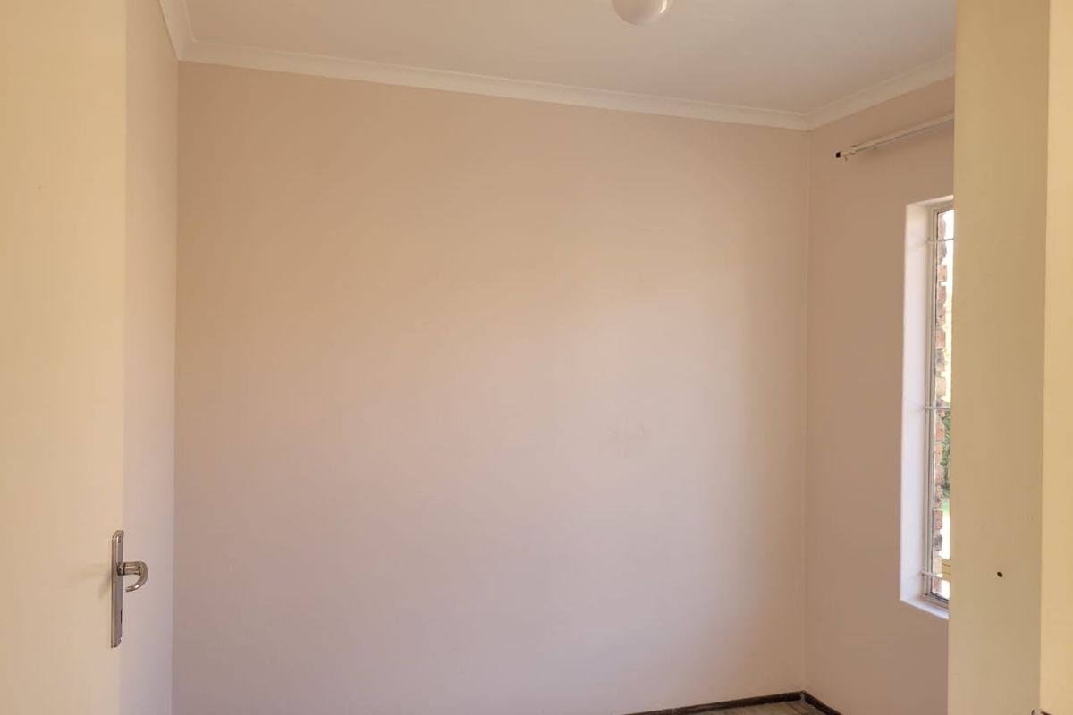 A clean, empty bedroom featuring neutral walls, tiled flooring, and a window fitted with security bars.