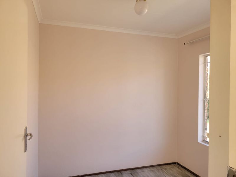 A clean, empty bedroom featuring neutral walls, tiled flooring, and a window fitted with security bars.
