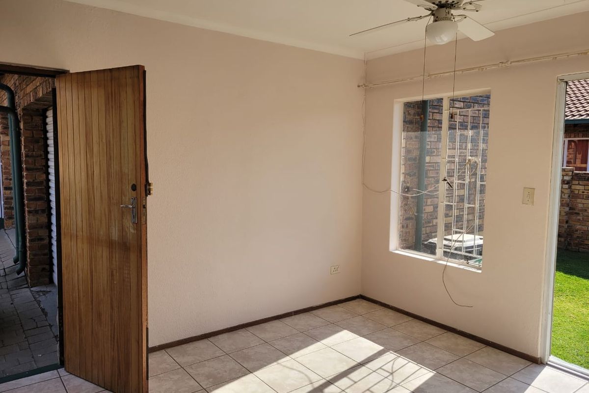 An empty living area featuring tiled flooring, a ceiling fan, and direct access to the garden through a sliding door.