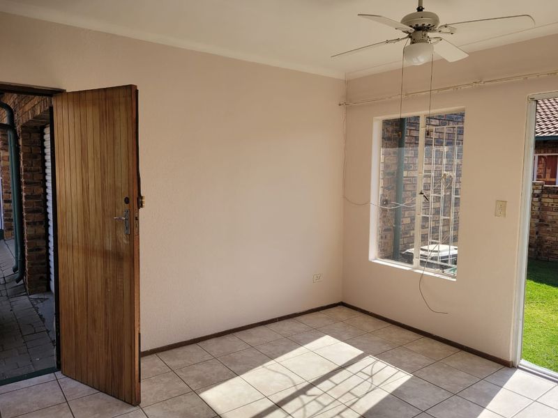 An empty living area featuring tiled flooring, a ceiling fan, and direct access to the garden through a sliding door.