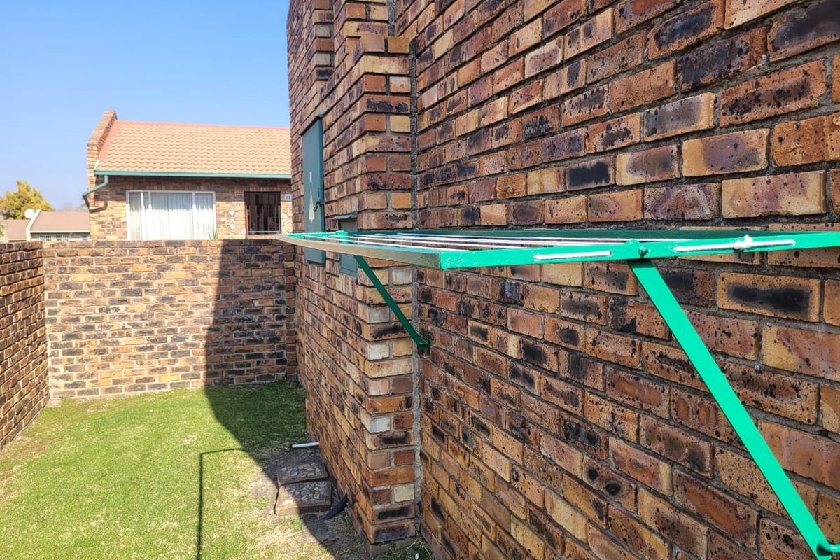 A rear exterior view of the townhouse featuring a face brick facade, a wall-mounted clothesline, and a small private lawn area.