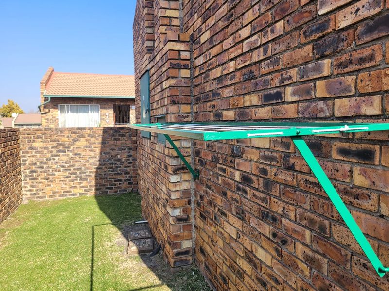 A rear exterior view of the townhouse featuring a face brick facade, a wall-mounted clothesline, and a small private lawn area.