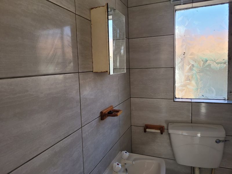A compact bathroom featuring tiled walls, a standard toilet, a basin, and a wall-mounted medicine cabinet with a frosted glass window.