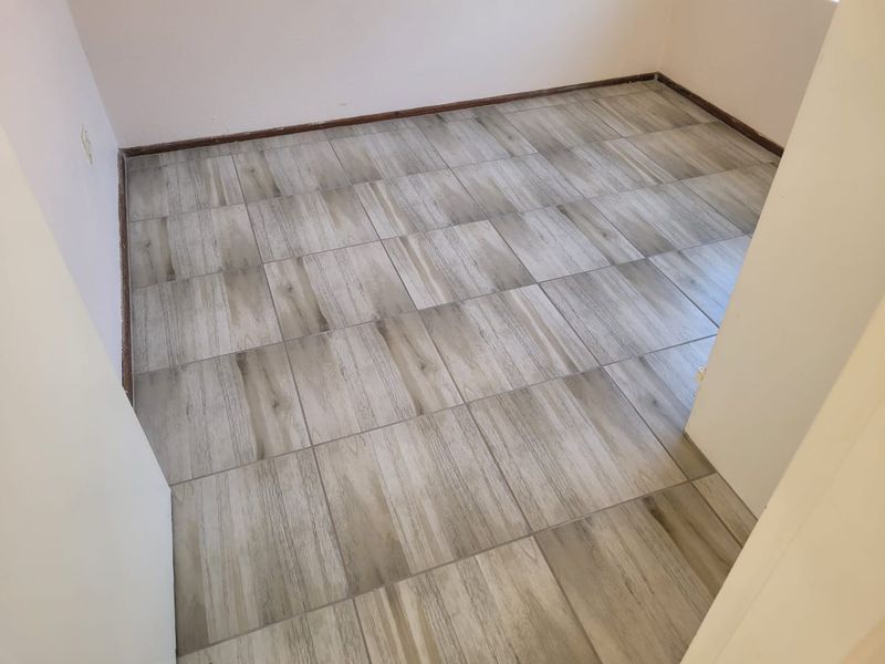 An empty bedroom featuring modern wood-look ceramic floor tiles and neutral wall finishes, ready for final touches and interior styling.