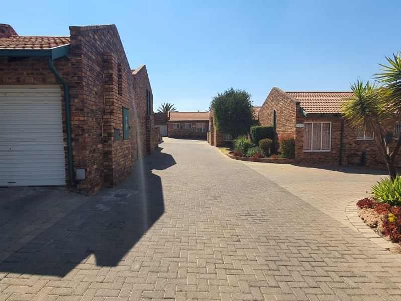 A view of the townhouse complex driveway featuring brick facades, tiled roofs, and paved access paths leading to individual garage units.