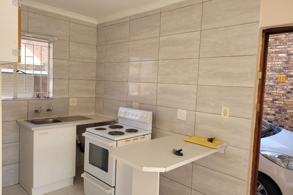 Compact kitchen featuring full-height wall tiling, a stainless steel sink, a freestanding stove, and a built-in breakfast bar.