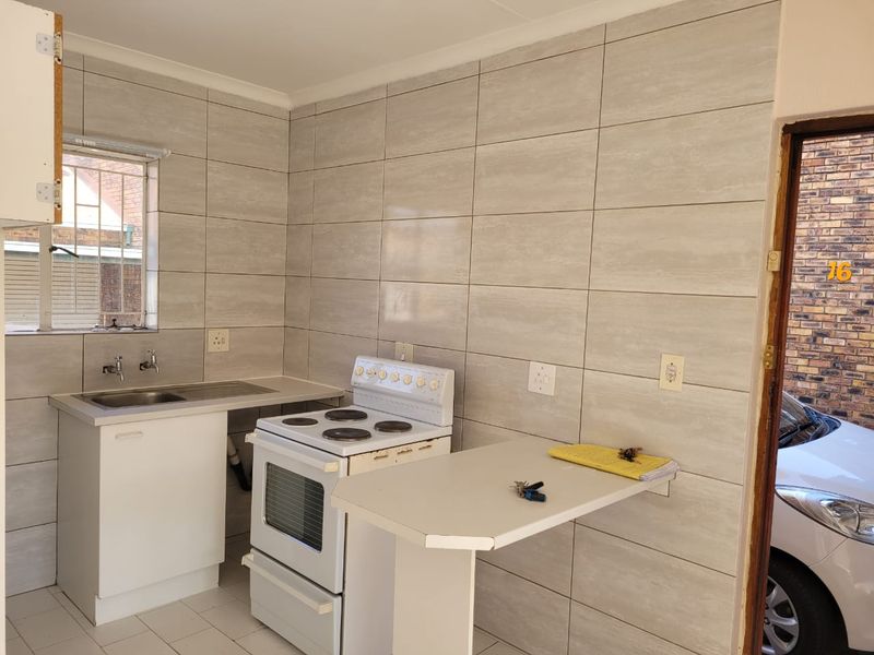 Compact kitchen featuring full-height wall tiling, a stainless steel sink, a freestanding stove, and a built-in breakfast bar.