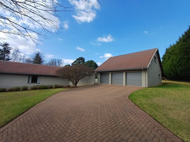 A well-maintained property exterior featuring a spacious paved driveway leading to a triple garage with tiled roofing and surrounding manicured lawns.