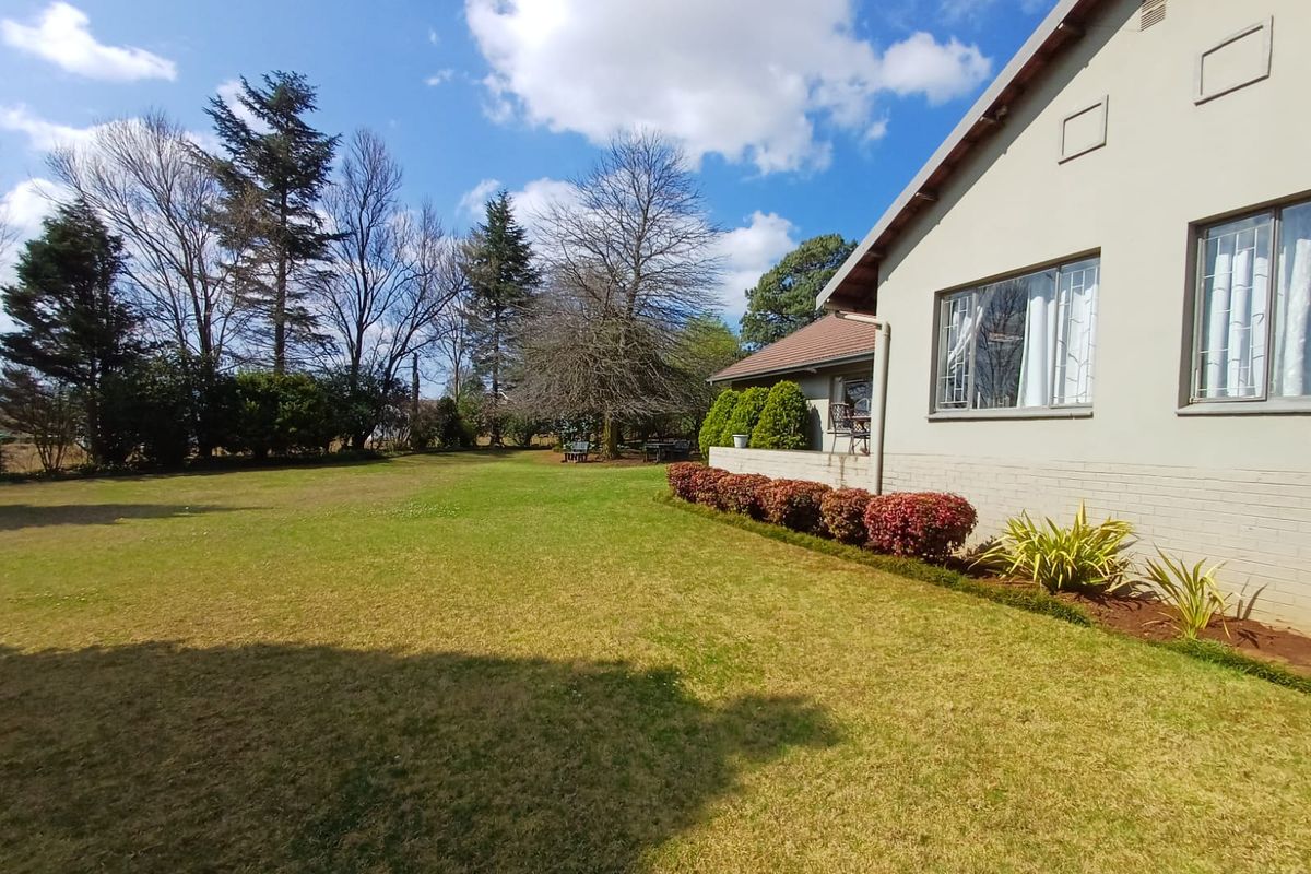 A well-maintained rear garden featuring a spacious lawn, established landscaping, and a view of the property's side elevation with brick and plaster finishes.