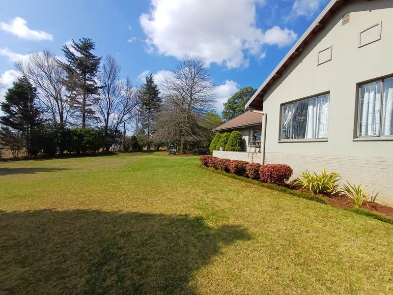 A well-maintained rear garden featuring a spacious lawn, established landscaping, and a view of the property's side elevation with brick and plaster finishes.