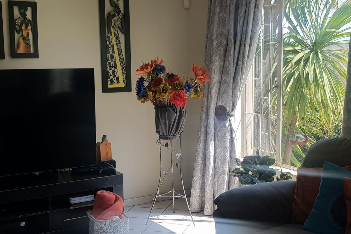 A living room area featuring tiled flooring and a window fitted with security bars, allowing natural light into the space.