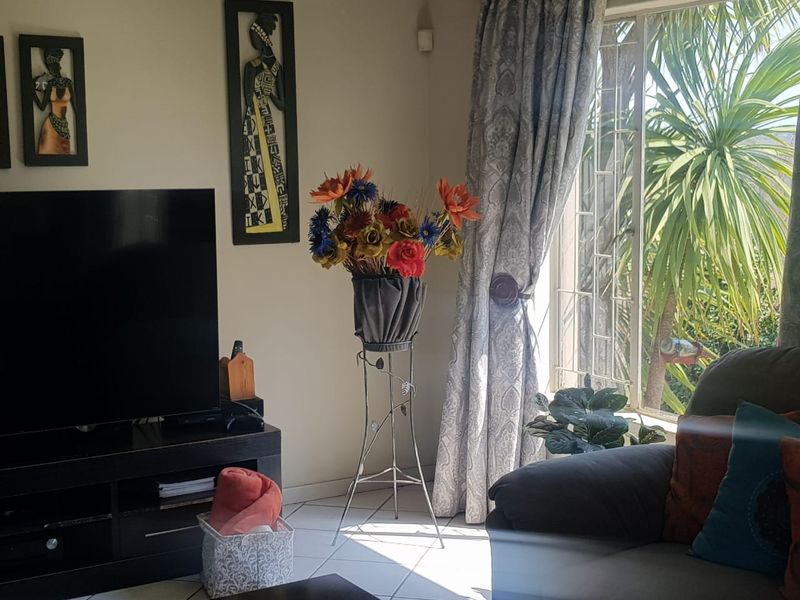 A living room area featuring tiled flooring and a window fitted with security bars, allowing natural light into the space.