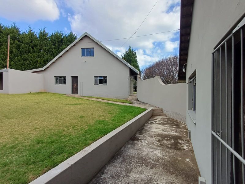 Rear view of the property featuring a concrete pathway, retaining wall, and a well-maintained lawn area with security bars on the windows.