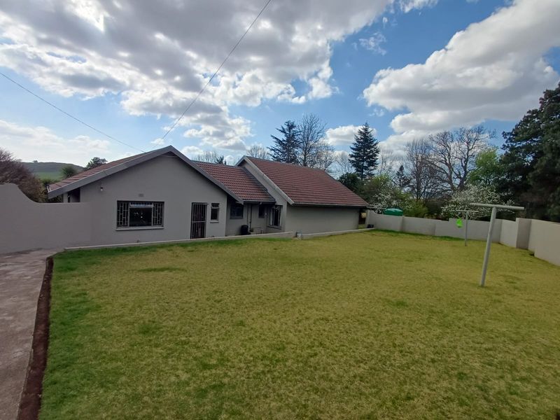 Rear view of the house featuring a spacious lawn, plastered exterior walls, tiled roof, and secure window bars.