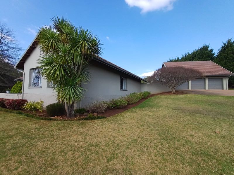 Rear view of the property featuring a well-maintained lawn, landscaped garden beds, and a detached triple garage with tiled roofing.