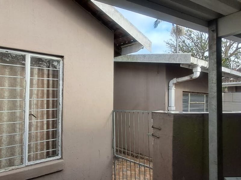 Rear exterior view of the cottage featuring a covered patio area, security bars on windows, and a metal access gate.