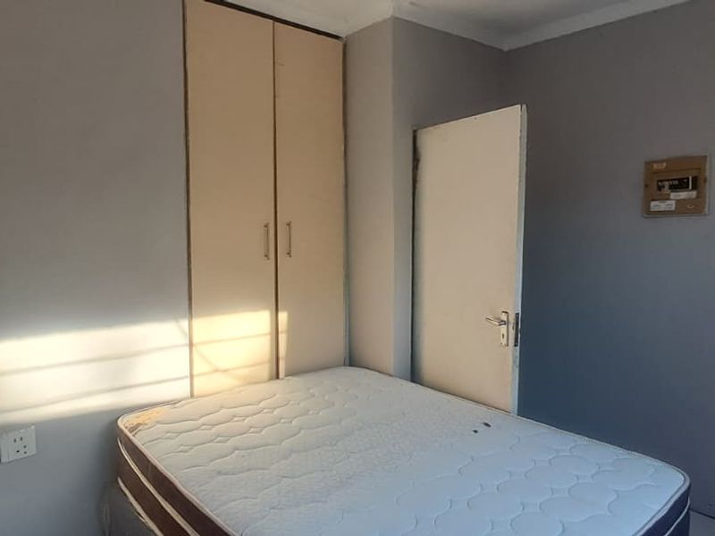 A bedroom featuring a built-in wardrobe, electrical distribution board, and neutral wall finishes, providing a functional space ready for cosmetic updates.