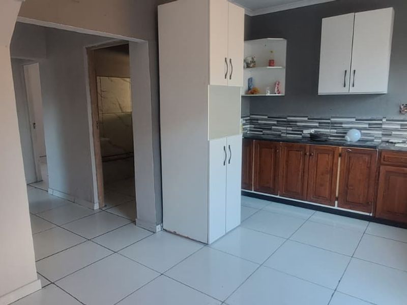 A functional kitchen space featuring tiled flooring, built-in wooden base cabinets, white overhead storage, and a double sink with a tiled backsplash.