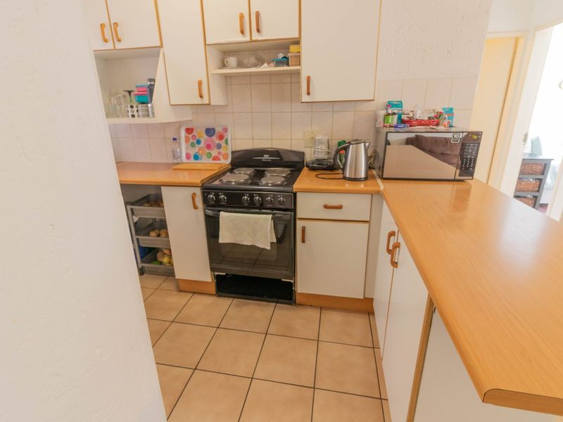 A compact kitchen featuring dated white cabinetry, laminate countertops, a freestanding stove, and tiled flooring, offering potential for a modern renovation.