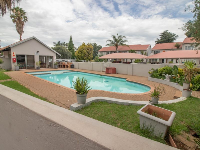 Communal swimming pool area featuring brick paving, a built-in braai, and surrounding perimeter walls within a townhouse complex.