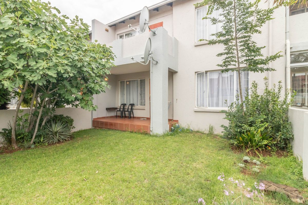 Rear view of the townhouse featuring a private garden, a tiled patio area, and established landscaping.