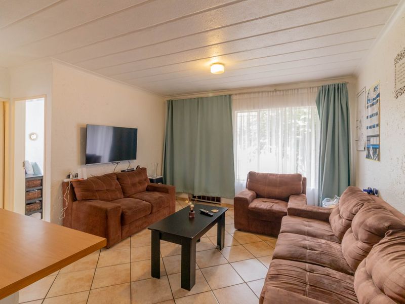 A comfortable living room featuring tiled flooring, textured walls, and a panelled ceiling, providing a functional and lived-in space.