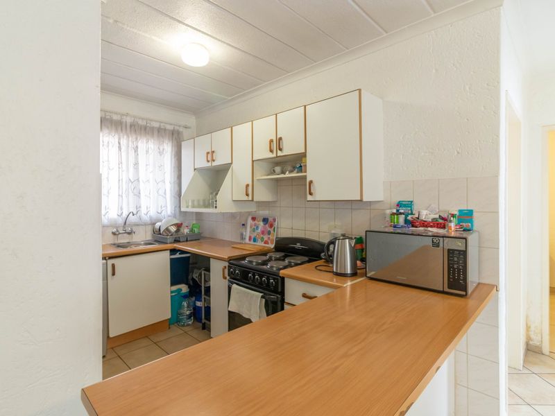 A compact kitchen featuring white cabinetry, laminate countertops, a tiled backsplash, and a freestanding stove, offering a functional layout with potential for modernization.
