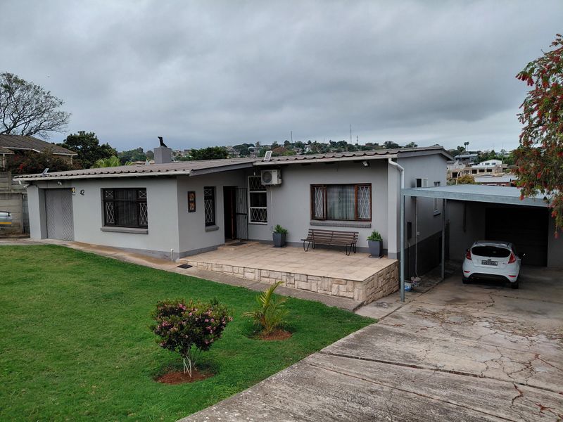 Front view of a single-story house featuring a tiled patio, stone cladding accents, a carport, and a well-maintained front lawn.