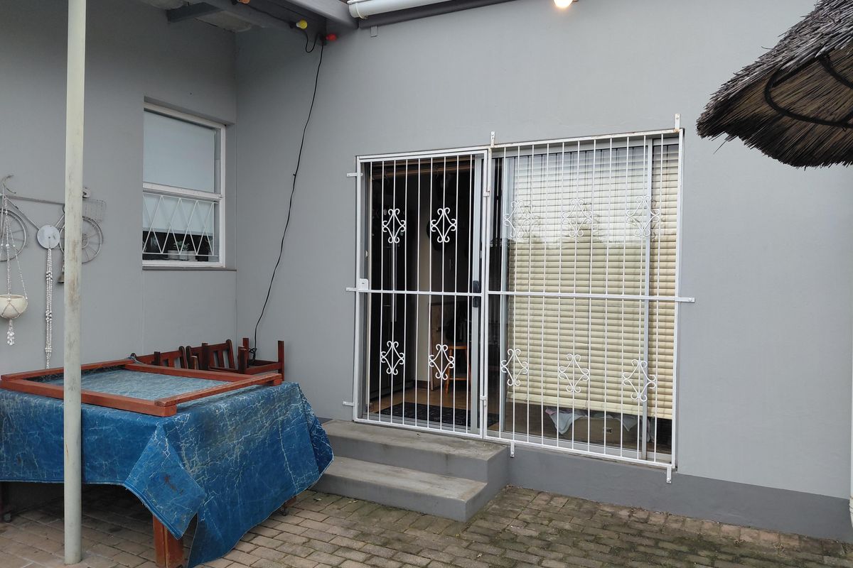 Rear exterior view featuring a paved patio area, security gate, and sliding door access to the home.