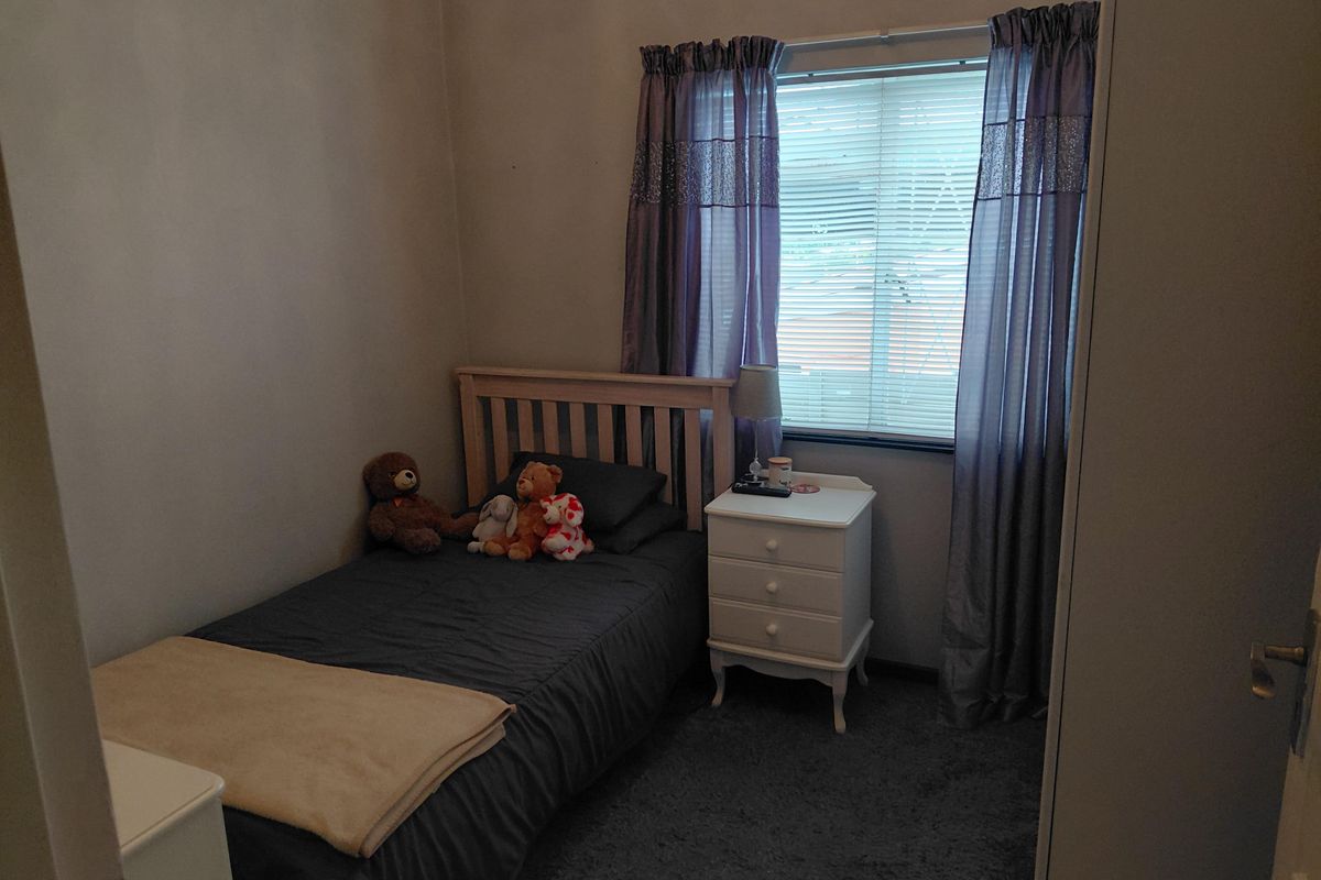 A compact bedroom featuring carpeted flooring and a window with fitted curtains.