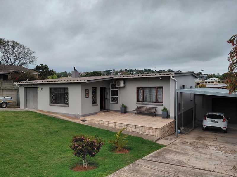Front elevation of a single-story house featuring a tiled patio, stone cladding accents, a carport, and a well-maintained lawn.