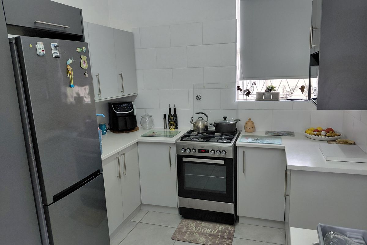 A functional kitchen featuring modern grey and white cabinetry, a gas stove with oven, tiled splashbacks, and neutral floor tiles.