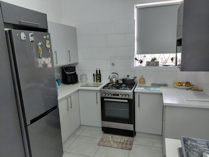 A functional kitchen featuring modern grey and white cabinetry, a gas stove with oven, tiled splashbacks, and neutral floor tiles.