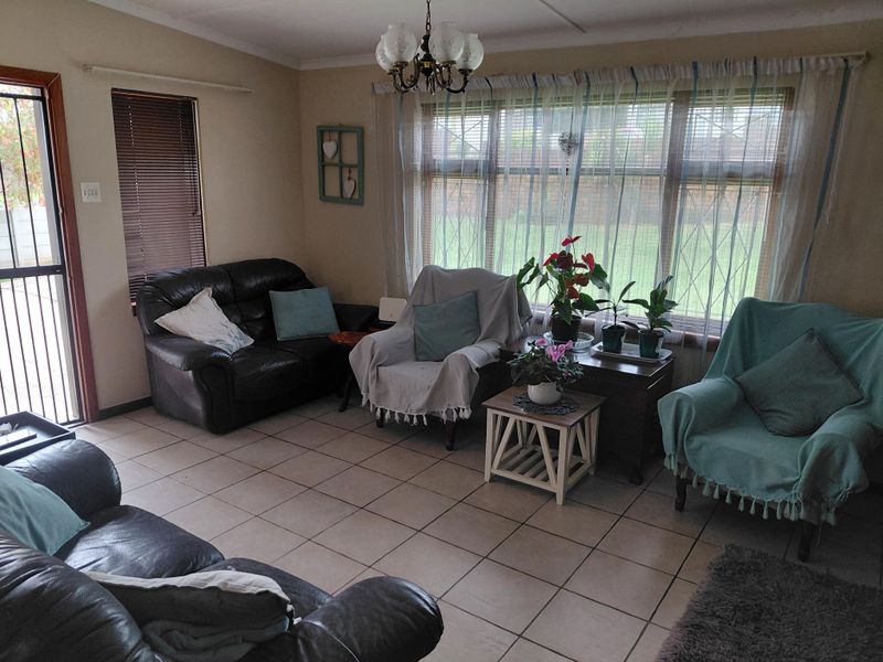 A living room featuring ceramic tile flooring, a large window with security bars, and a ceiling-mounted chandelier.
