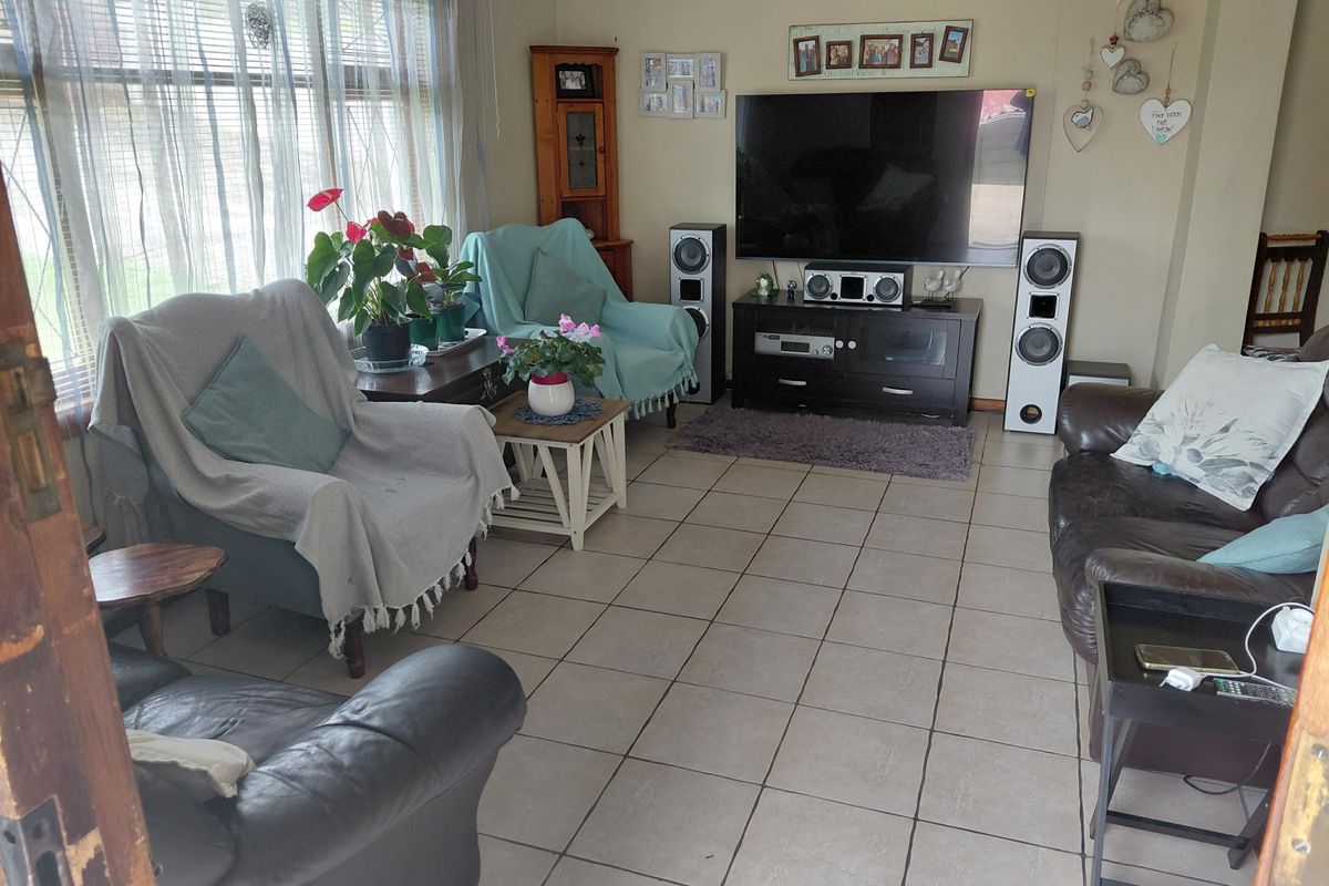 A comfortable living room featuring tiled flooring and a large window with venetian blinds, providing ample natural light.